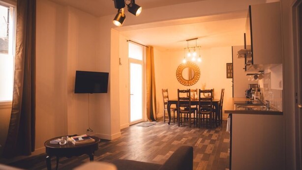 A living room with a TV, a dining area with a circular mirror, and a kitchen with a refrigerator. - Le Cube Soma - Large T3 (Tours)