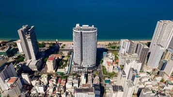 A high-rise building with a circular design, surrounded by other tall buildings, near a coastline.
