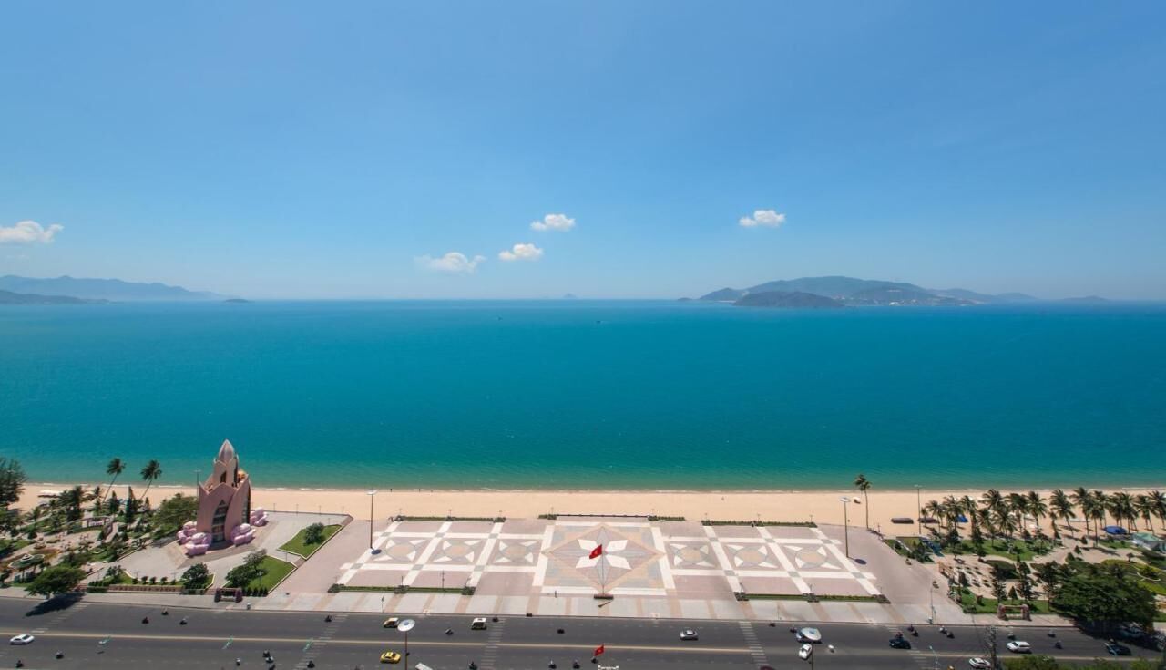 A coastal view with a large open plaza, a distinctive building with a pointed roof, and a clear blue sea.