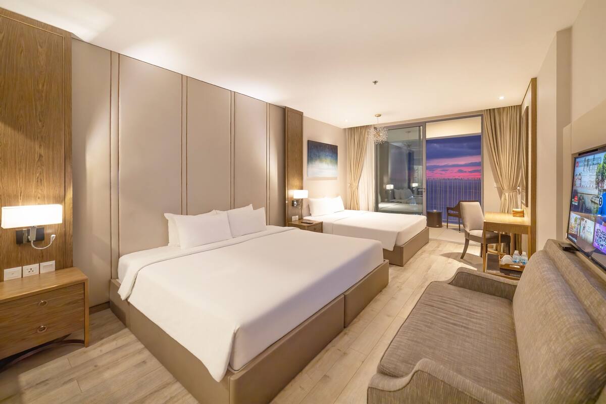Quarto de hotel com uma cama grande, um sofá, uma escrivaninha e uma televisão.