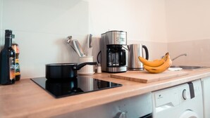 A kitchen with a coffee maker, a pot, a bottle, a banana, and a sink.