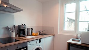 A compact kitchen with a washing machine, a coffee maker, and a window providing natural light.