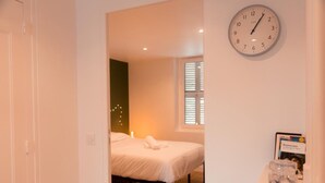 A bedroom with a bed, a clock, and a window with blinds.