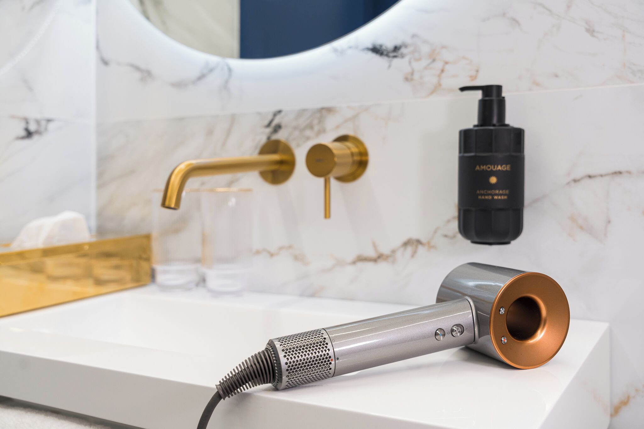A bathroom with a marble sink, gold faucet, and a hairdryer on the counter.