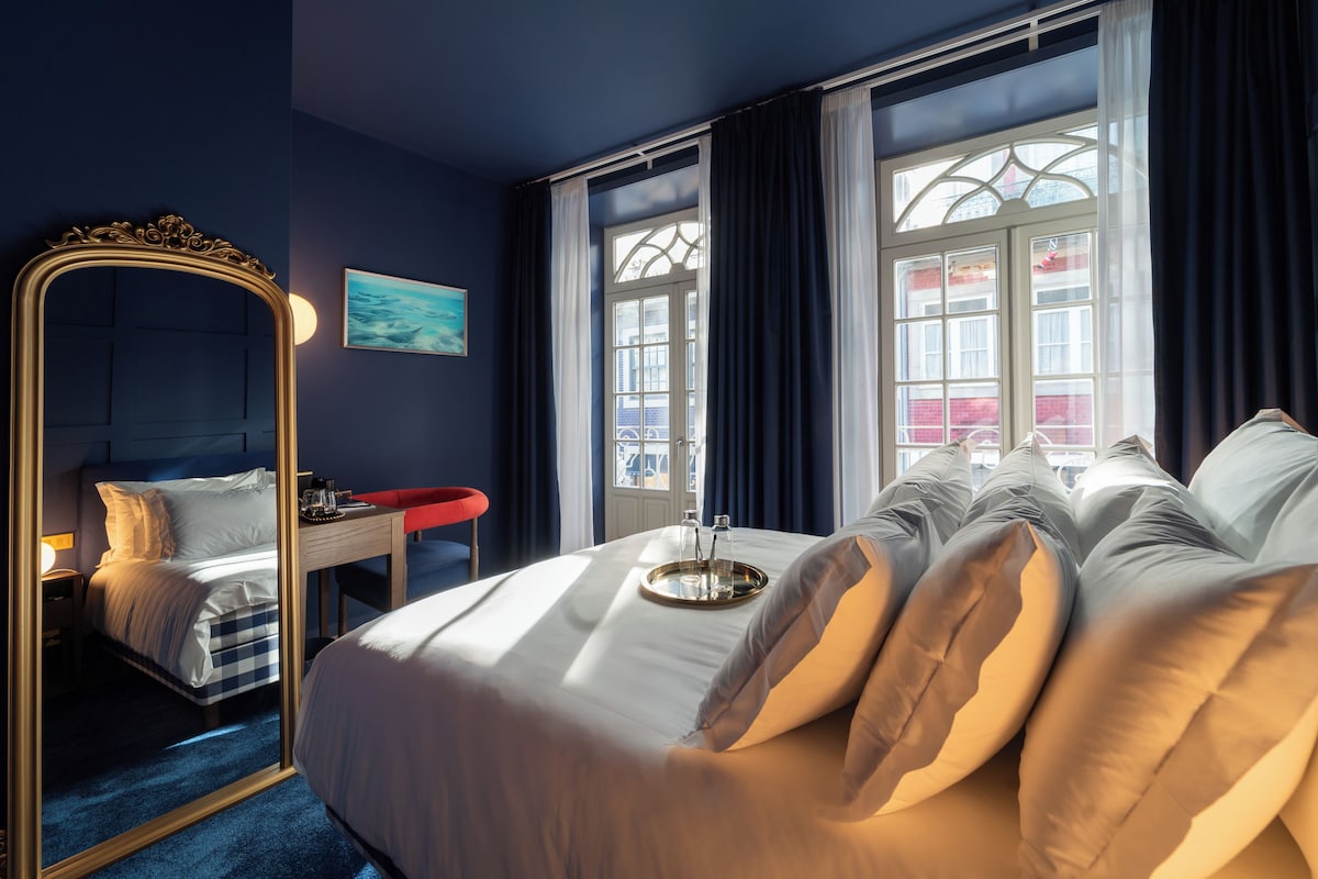 Une chambre d’hôtel avec un grand lit, un miroir, un bureau et une fenêtre avec des rideaux.