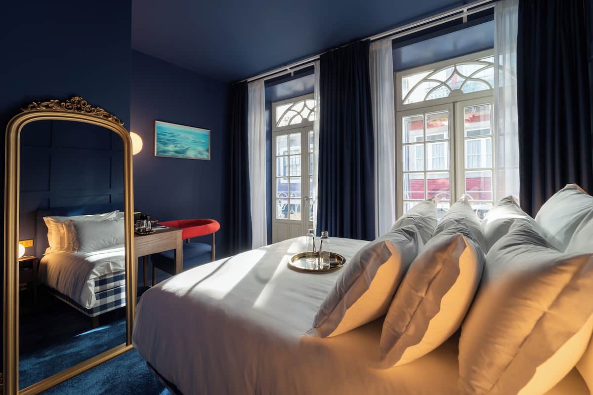 Habitación de hotel con cama, espejo, escritorio y ventana con cortinas.