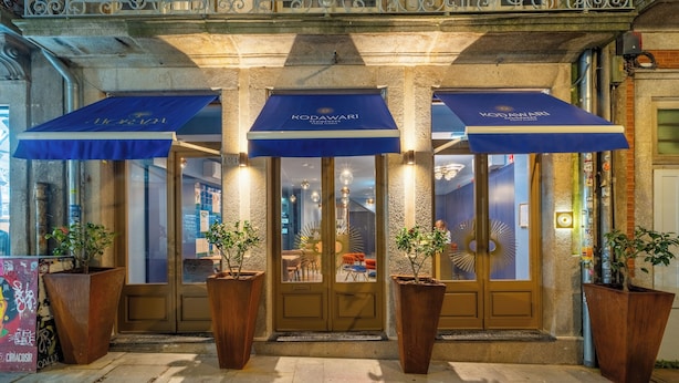 L’entrée d’un hôtel, avec des auvents bleus, de grands pots de plantes et une façade en pierre.