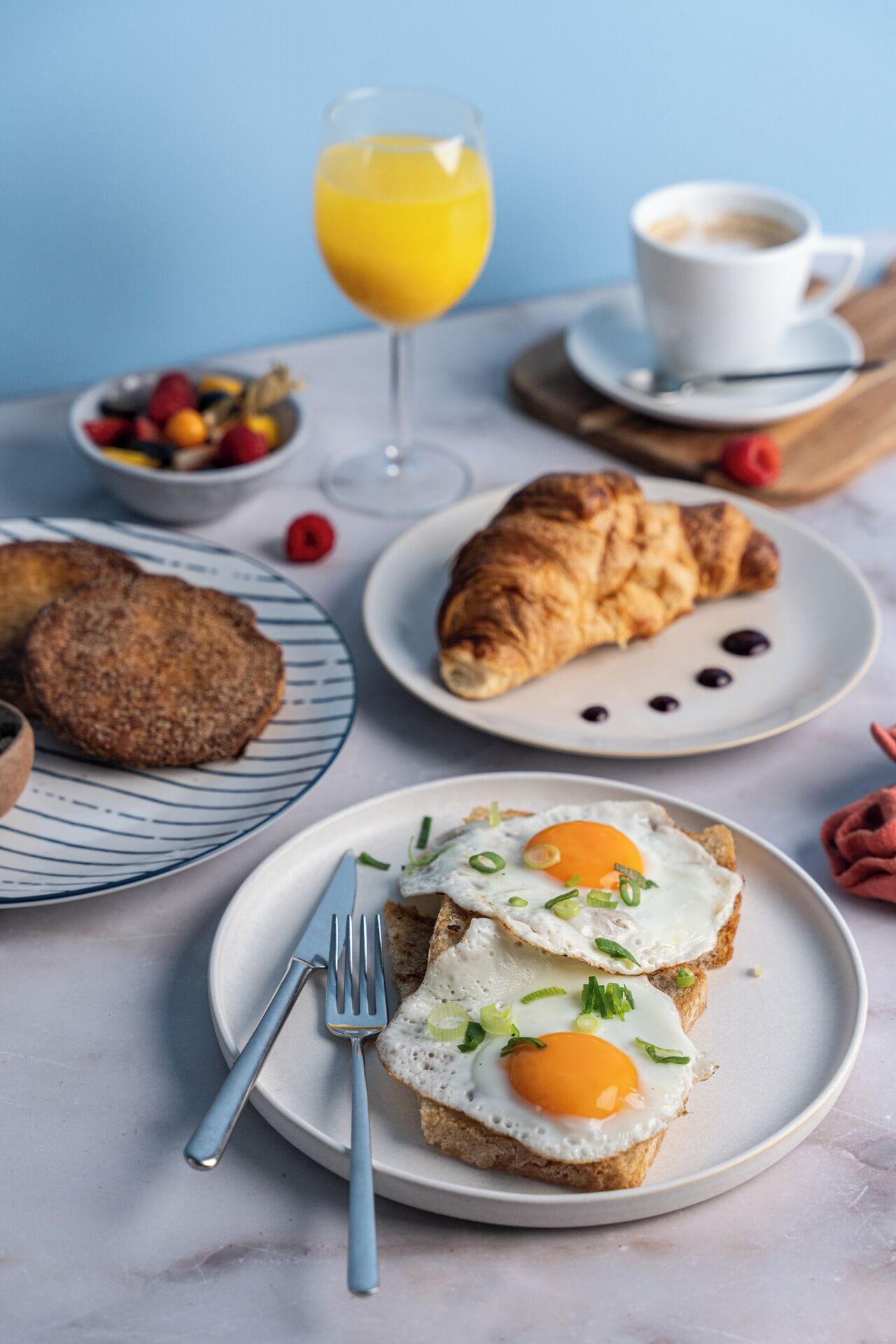 A breakfast setting with croissants, eggs, and a glass of orange juice on a table.