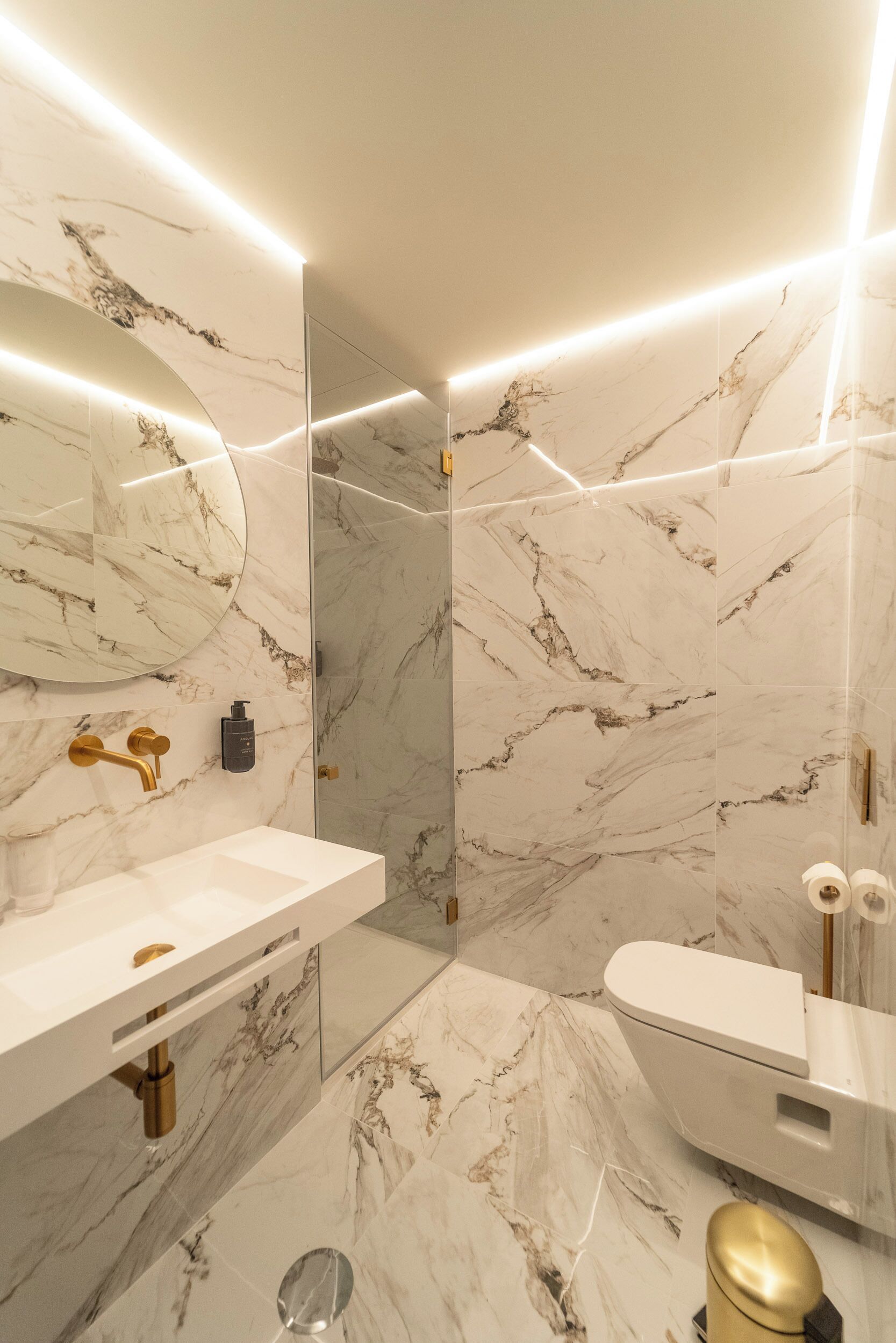 A modern bathroom with marble walls, a white sink, and a toilet.