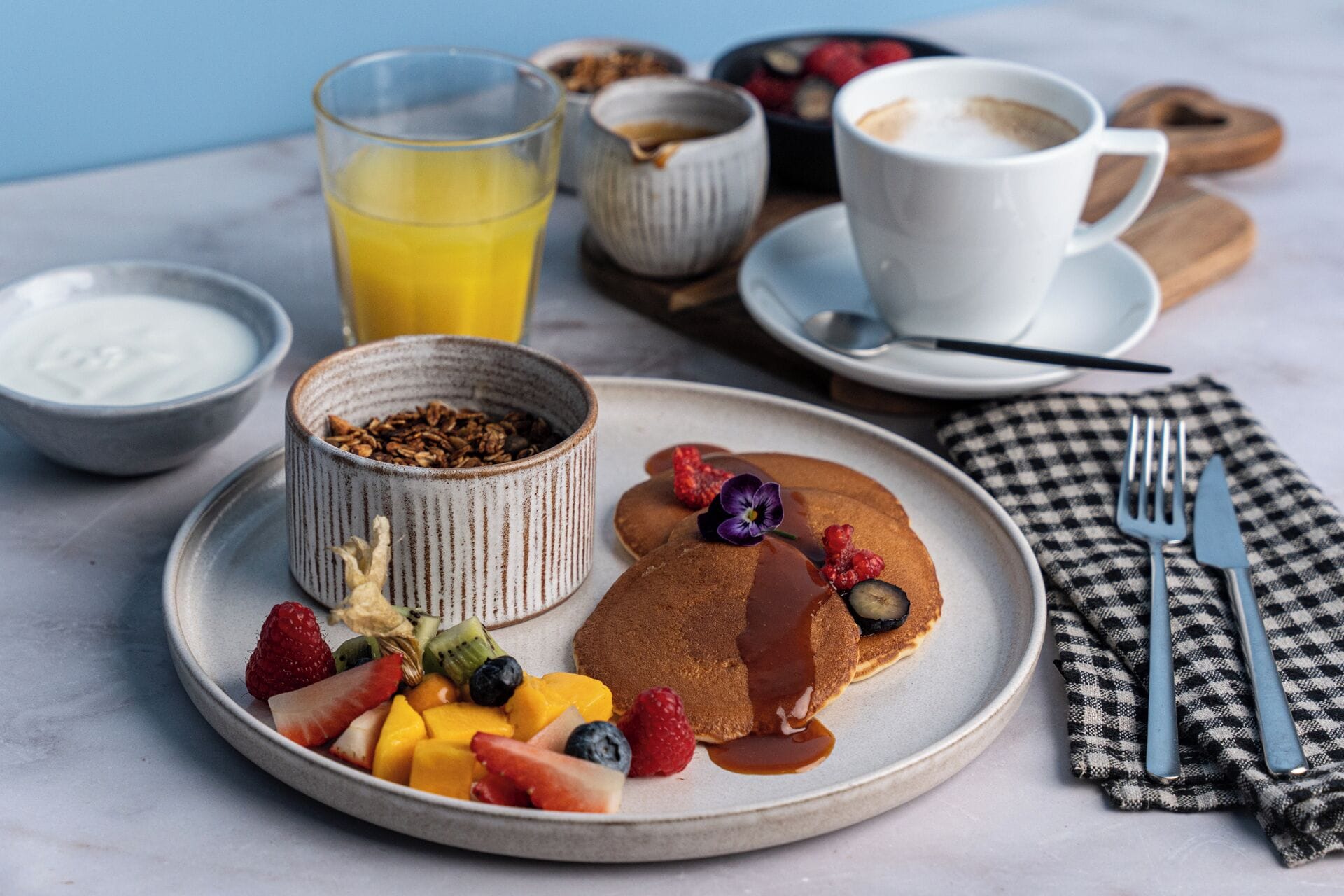 A breakfast plate with pancakes, berries, and syrup, a glass of orange juice, and a cup of coffee on a table.