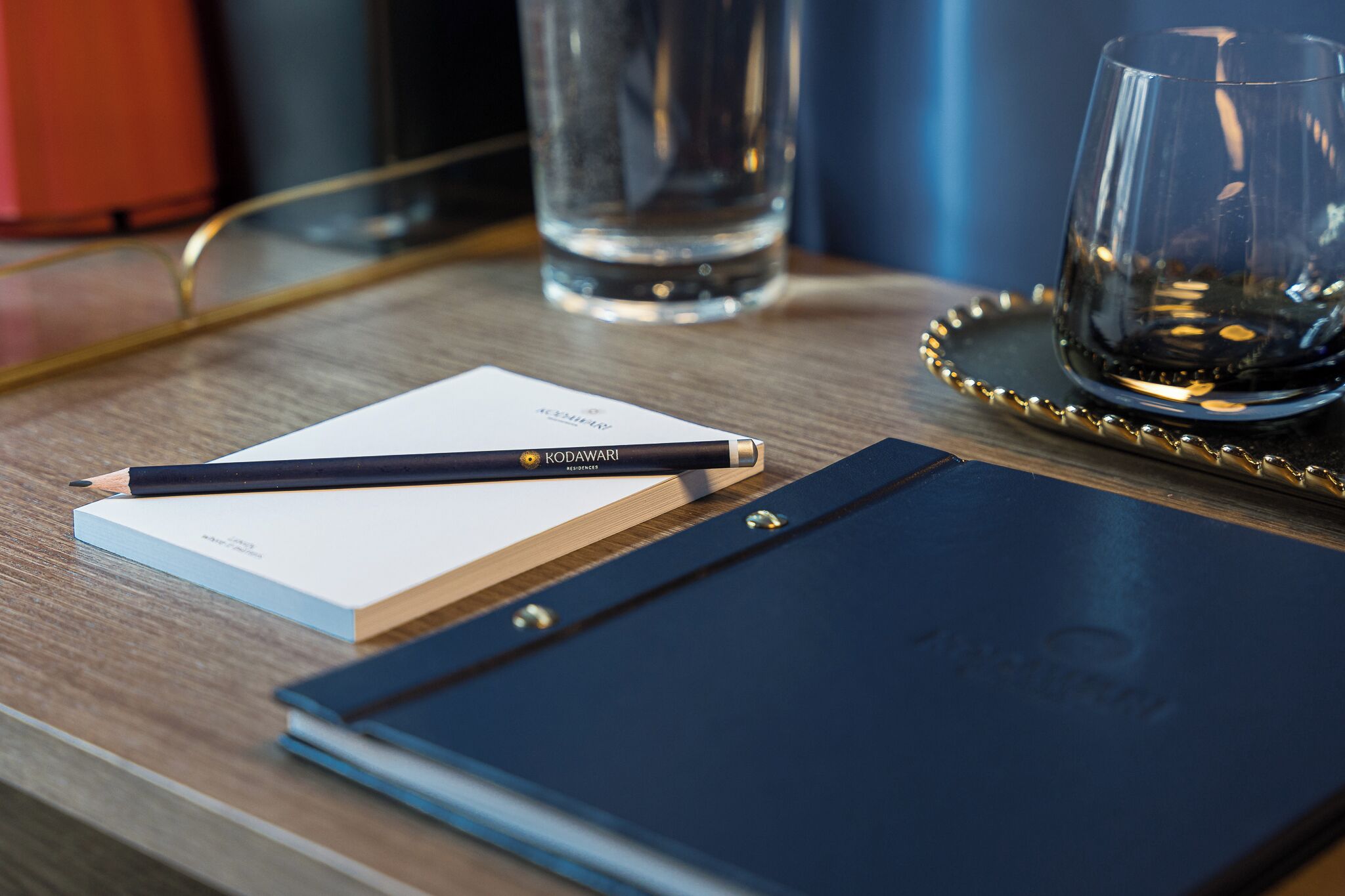 A wooden table with a notebook, a pencil, a glass of water, and a glass of wine.