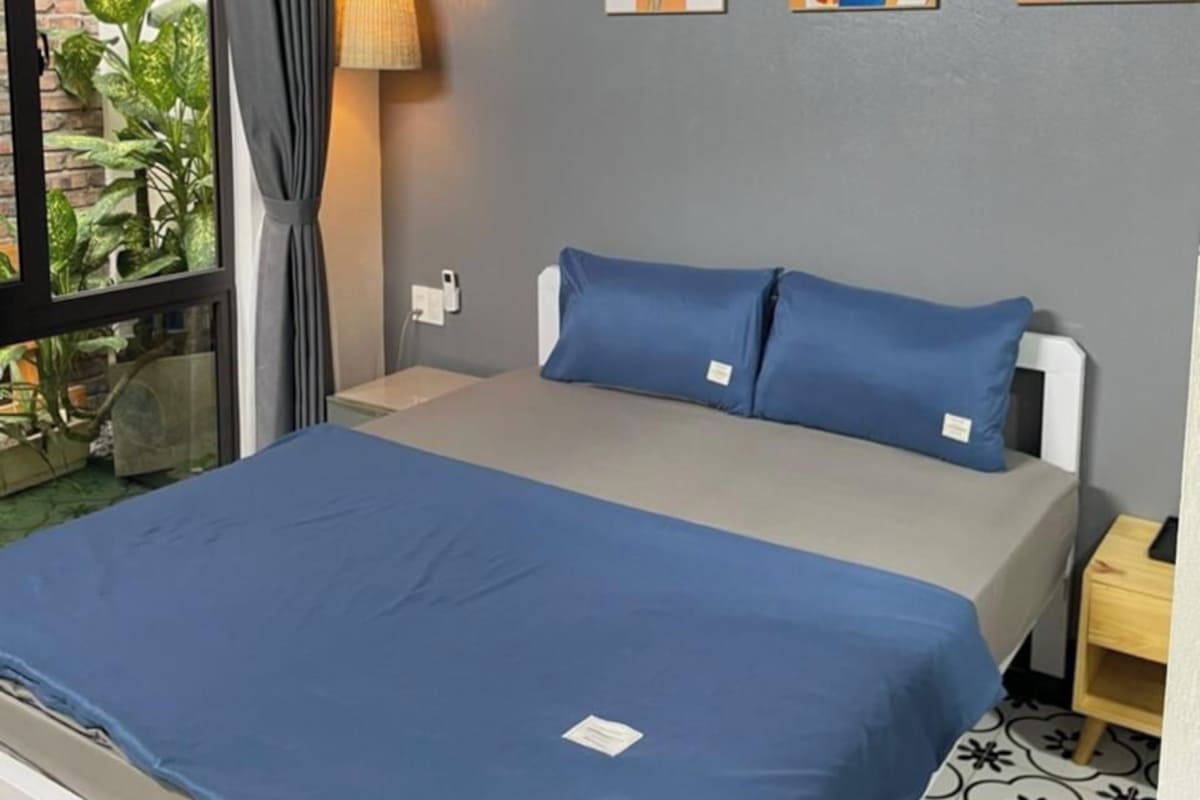 Quarto com cama, janela com cortinas, luminária na parede e três obras de arte emolduradas.