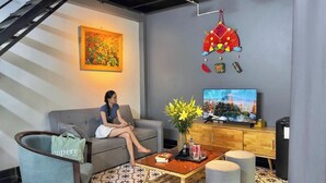 Un soggiorno con divano, tavolino da caffè con un libro e una pianta, televisione e un ornamento decorativo appeso.