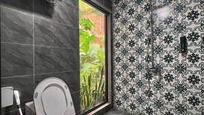 Un bagno con il water, una doccia e una finestra con vista sul verde.