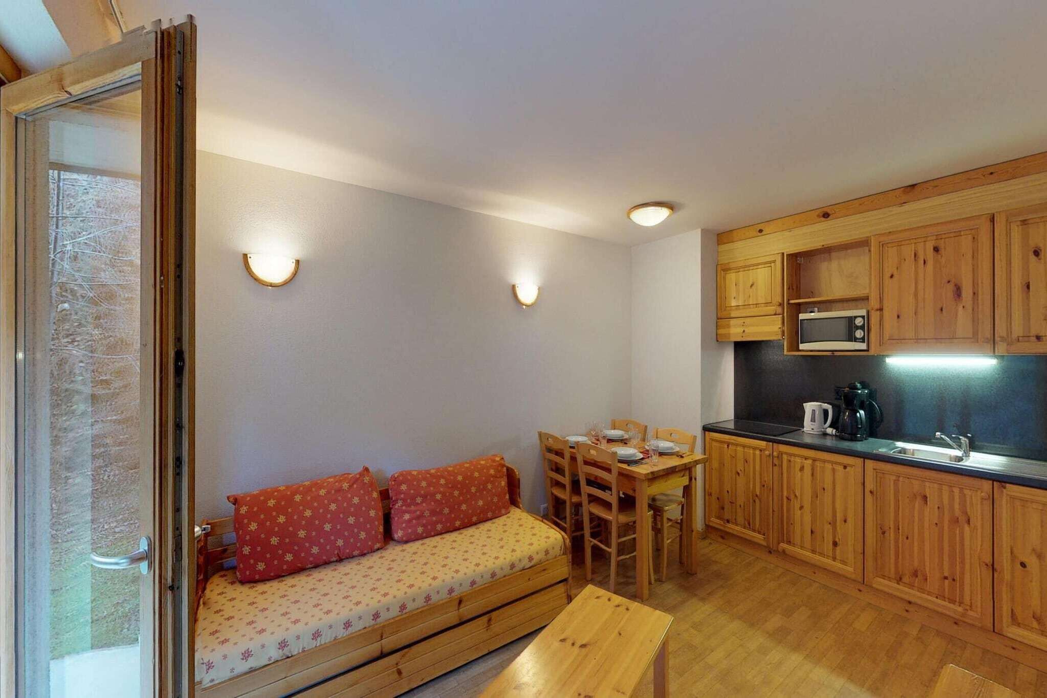 A compact room with a wooden sofa, dining table, and kitchenette.