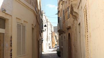 A narrow street with buildings on both sides, featuring balconies and shutters.