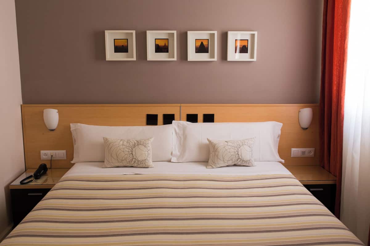 Une chambre d’hôtel avec un lit, des tables de chevet, un téléphone et des tableaux encadrés au mur.