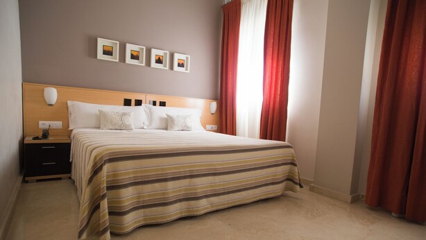A hotel room with a bed, nightstands, and a wall with framed pictures. - Hostal Albero by eme hoteles (Sanlucar la Mayor)