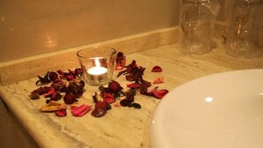 A bathroom with a marble countertop, a lit candle, and scattered dried rose petals. - Hostal Albero by eme hoteles (Sanlucar la Mayor)