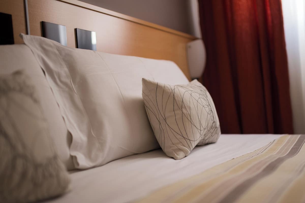 Un lit avec une tête de lit en bois, deux oreillers et une couvre-lit à rayures.