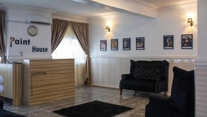 A reception area with a wooden reception desk labeled "RECEPTION" and "Paint House." There are framed pictures on the wall and a black armchair.
