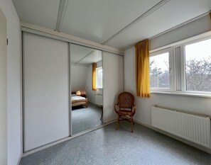 A room with a large sliding door, a single window with yellow curtains, a radiator, and a wooden chair. - Holiday Bungalow With Wifi Near Beach (Sint Maartensvlotbrug)
