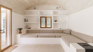 A modern living room with a built-in sofa, white shelving, a wooden-framed window, and a small potted plant.