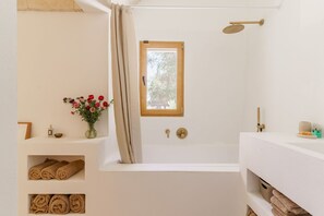 Un baño con bañera, ventana, ducha y toallas en estantes.