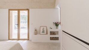 A bedroom with a large sliding glass door leading to an outdoor area, a bed, a small shelf with decorative items, and a wall-mounted shelf with rolled towels.