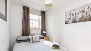 A bedroom with a bed, curtains, a nightstand, a lamp, and a wall-mounted painting. - Stunning 1 bedroom short term let in Aberdeen city center close to all amenities (Aberdeen)