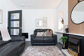 A living room with a sofa, a chair, a fireplace, and framed artwork on the wall.