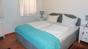 Une chambre à coucher avec un lit, deux tables de chevet, une lampe et une fenêtre avec des stores.