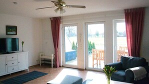 Un salon équipé d’un téléviseur, d’un ventilateur de plafond, d’un canapé, d’une table basse et offrant une vue sur l’extérieur grâce à une porte-fenêtre coulissante.