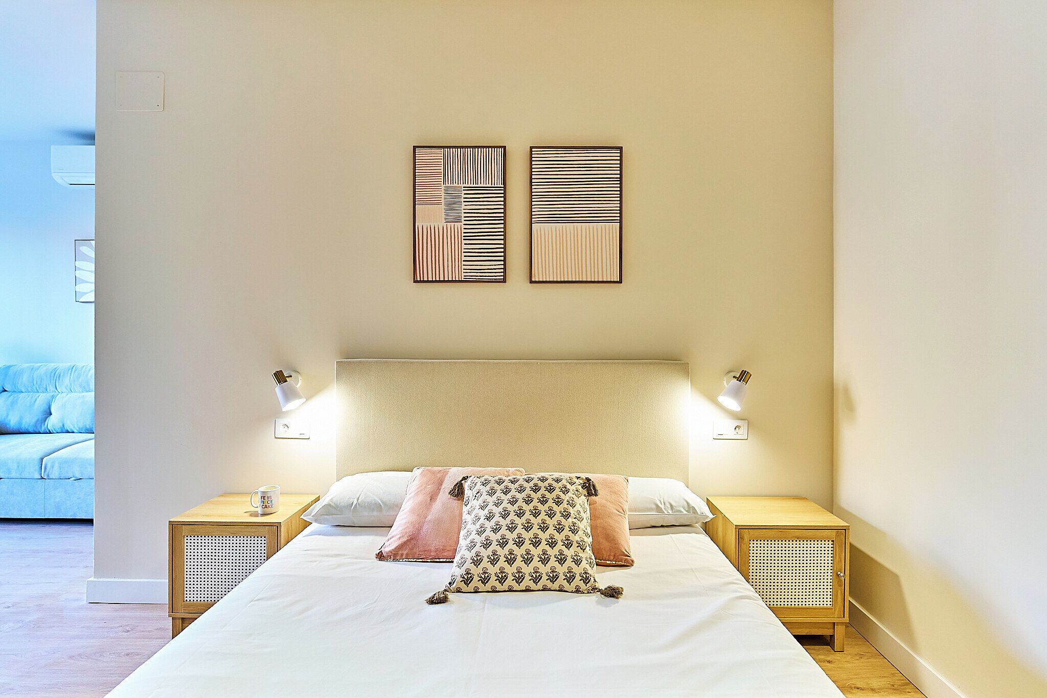 A neatly made bed with a patterned pillow, two bedside tables with lamps, and two wall-mounted artworks.