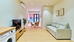 Un apartamento moderno con lavadora, sofá, zona de comedor con sillas y televisor.