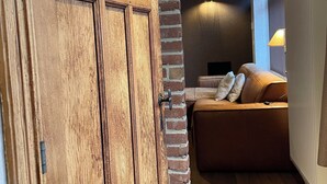 Uma porta de madeira com um painel de vidro, parede de tijolos, sofá com almofadas e um abajur.