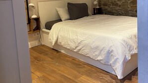 Quarto com cama, mesa de cabeceira, abajur e parede de pedra.