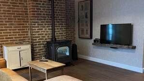 Uma sala de estar com parede de tijolos, piso de madeira, sofá, mesa, televisão e lareira.