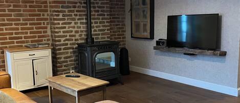 A living room with a brick wall, a wooden floor, a sofa, a table, a TV, and a fireplace.