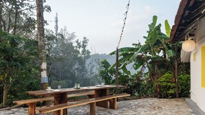 A wooden picnic table with benches, surrounded by a tiled patio and lush greenery. - Last Villa (Madikeri)