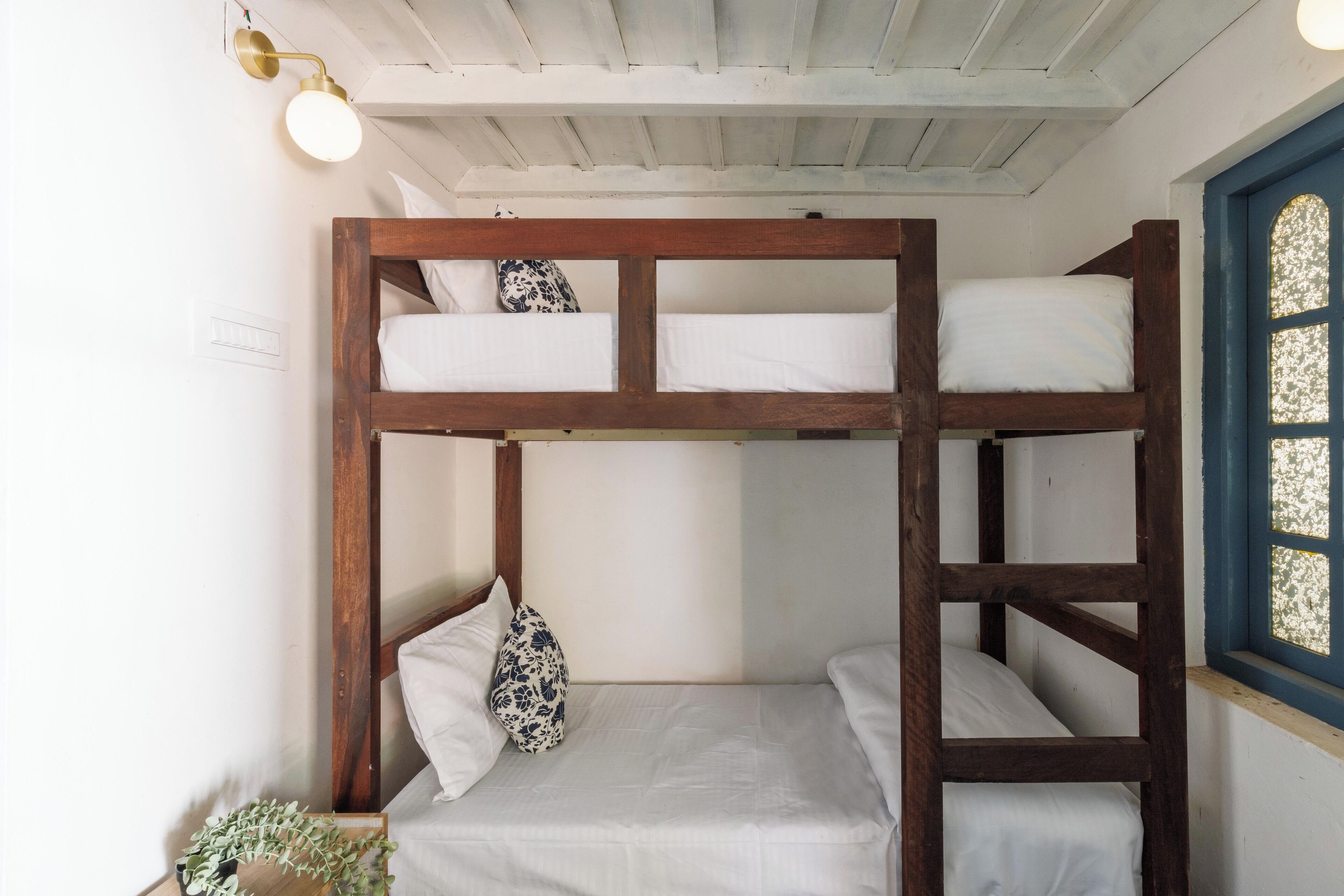 A bunk bed room with white bedding, a wooden headboard, and a small plant on the floor.