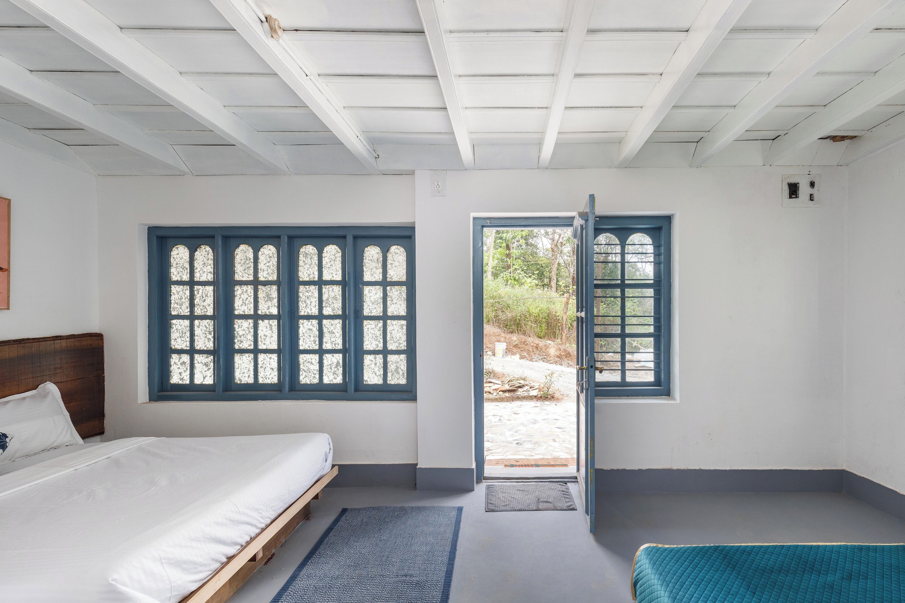 Een slaapkamer met een bed, een raam met blauwe luiken en een deur naar buiten.