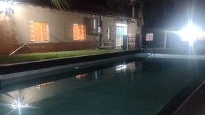 Vista nocturna de una piscina con un edificio al fondo.