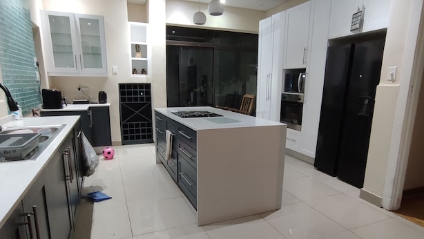 Una cocina moderna con una isla central, muebles blancos y un refrigerador negro.