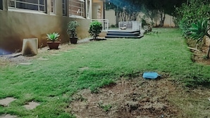 Una casa con césped cuidado, algunas plantas en macetas y un perro visible en el porche.