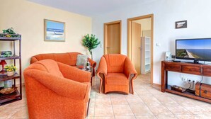 A living room with two orange armchairs, a wooden TV stand, and a bookshelf. - Cozy vacation apartment with balcony near the beach and center (Ückeritz)