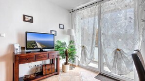 A living room with a TV, wooden entertainment unit, potted plants, and a view through a window with sheer curtains. - Cozy vacation apartment with balcony near the beach and center (Ückeritz)