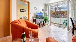 A living room with a sofa, a table with a bottle and glasses, a TV, and a balcony with a view. - Cozy vacation apartment with balcony near the beach and center (Ückeritz)