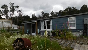 A rustic cabin with a wooden deck, surrounded by wildflowers and native vegetation.