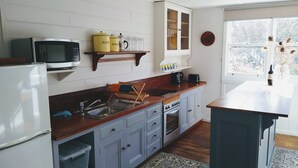 A kitchen with white cabinets, a wooden countertop, a built-in oven, a microwave, and a window with a view of trees.